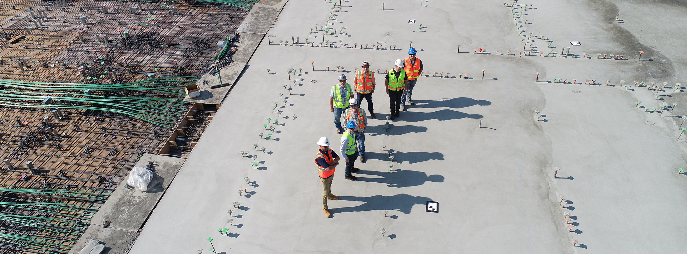 View from above of 7 men in safety vests and hardhats on a construction site.