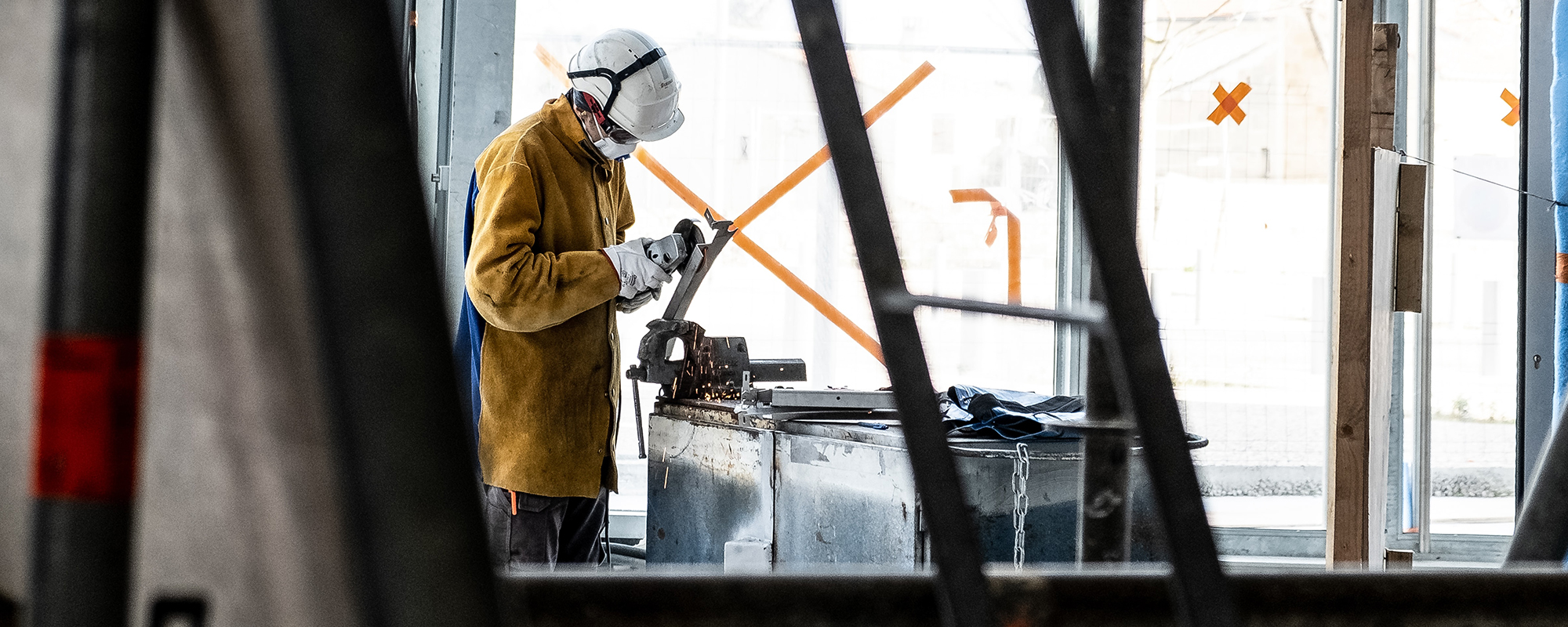 Industrial job worker wearing COVID mask and white hard hat in industrial setting while cutting metal