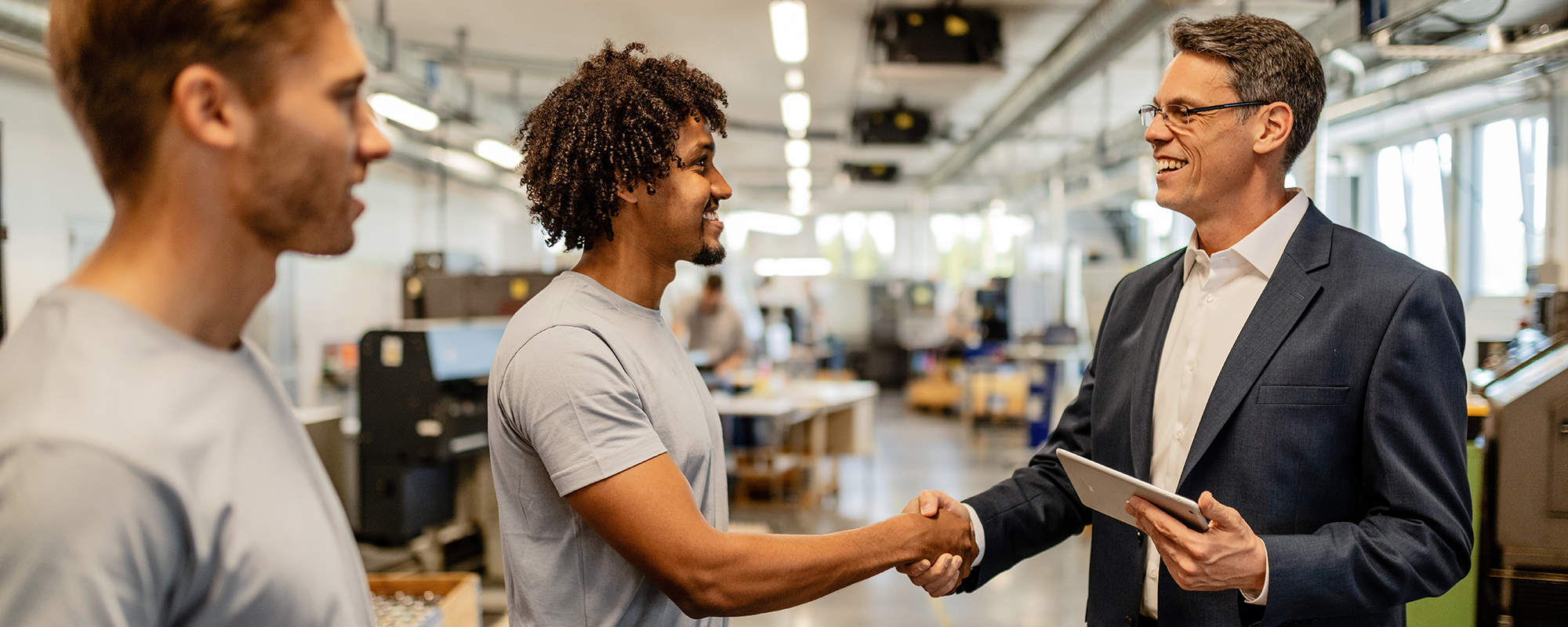 Man in business attire greeting an African American man in a gray t-shirt in an office setting