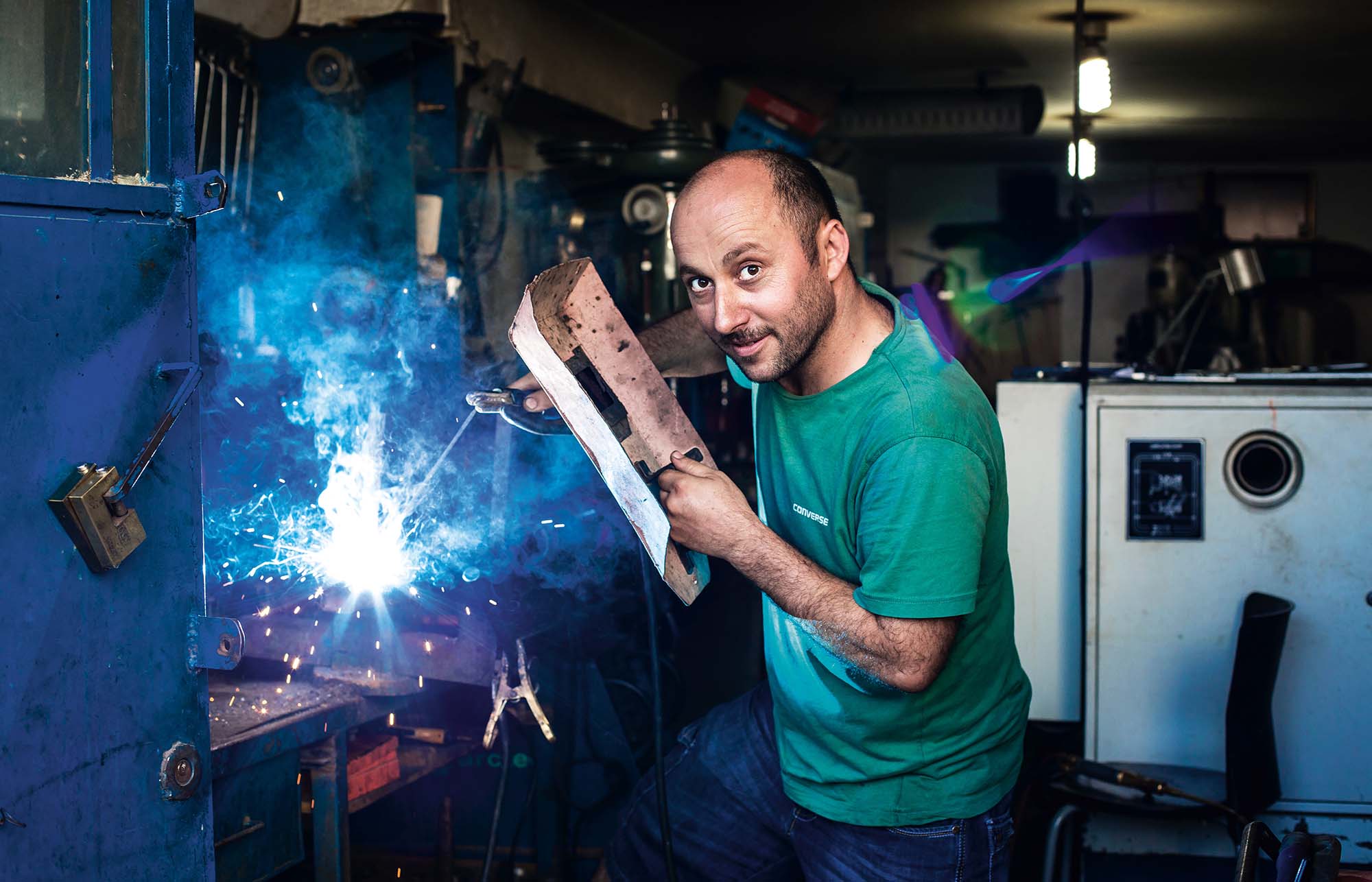 Man smiling behind welding mask as he turns to look at camera while working on industrial job